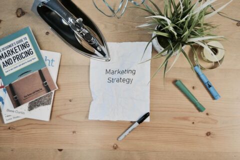 A white colored paper with text Marketing strategy along with a pen