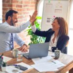 Two working professionals celebrating their success at work by giving a high five