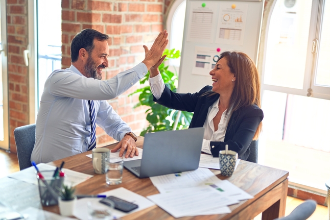 Two working professionals celebrating their success at work by giving a high five